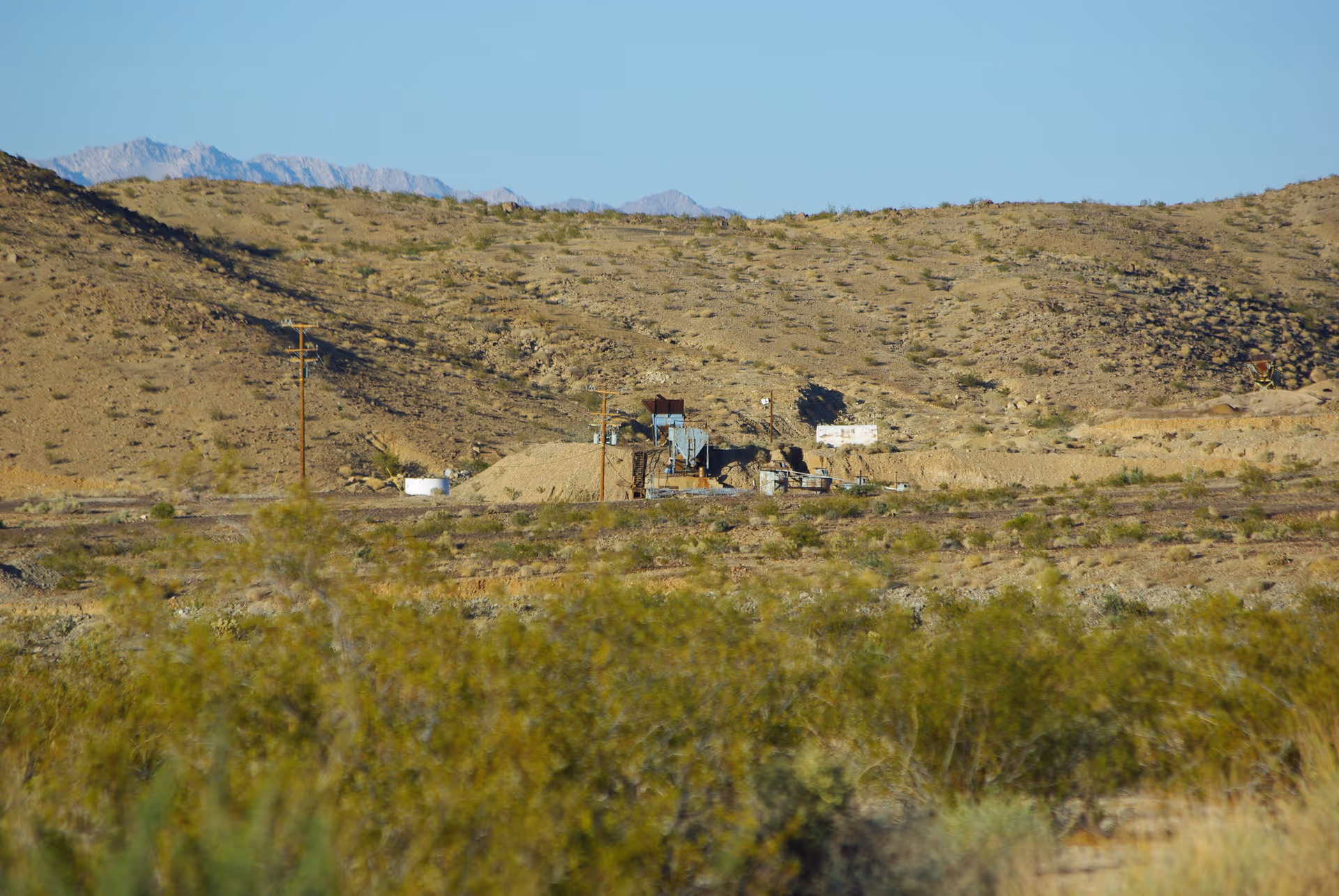 Desert landscape with distant hills and a small, weathered industrial facility.
