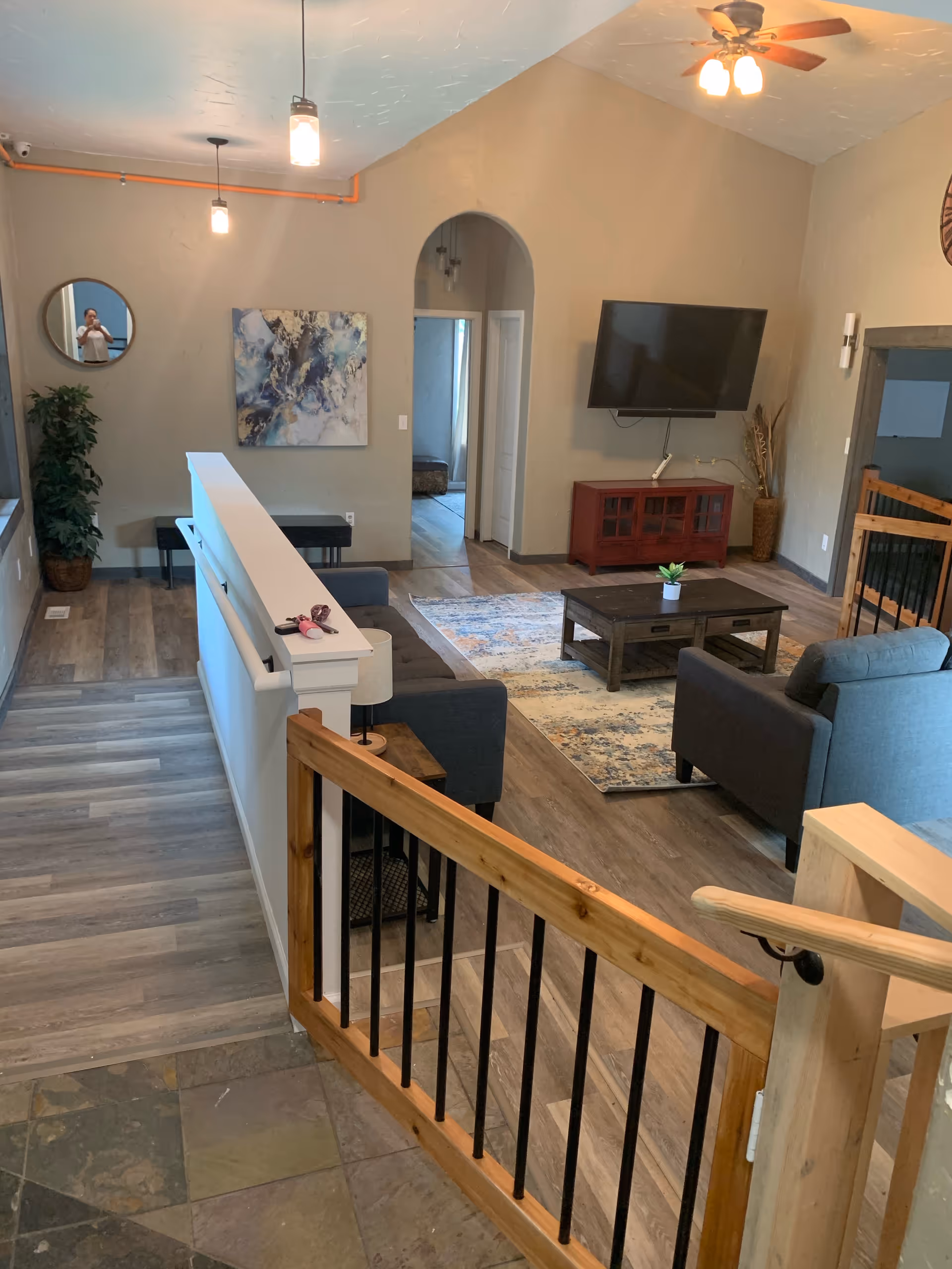 Open living room with gray couches, coffee table, rug, mounted TV, and staircase railing.