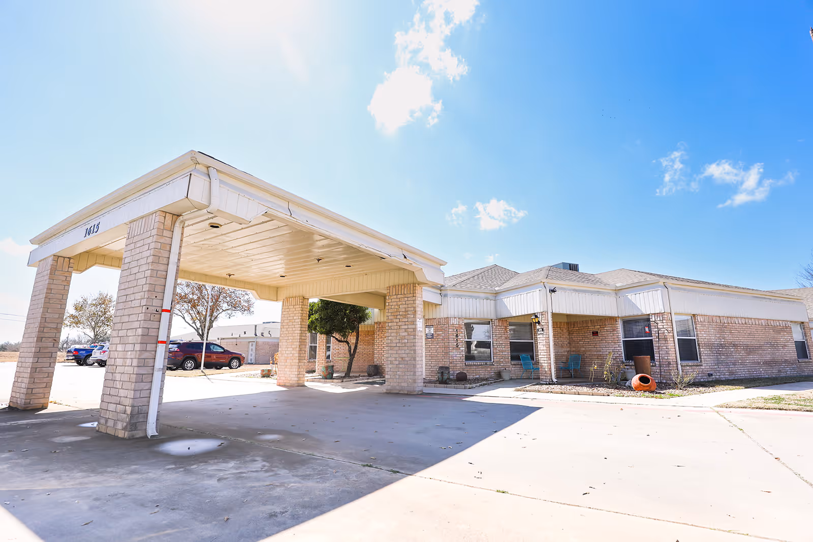 Front exterior of a single-story brick rehabilitation and healthcare center with a covered drive-through entrance and parking lot under a blue sky.