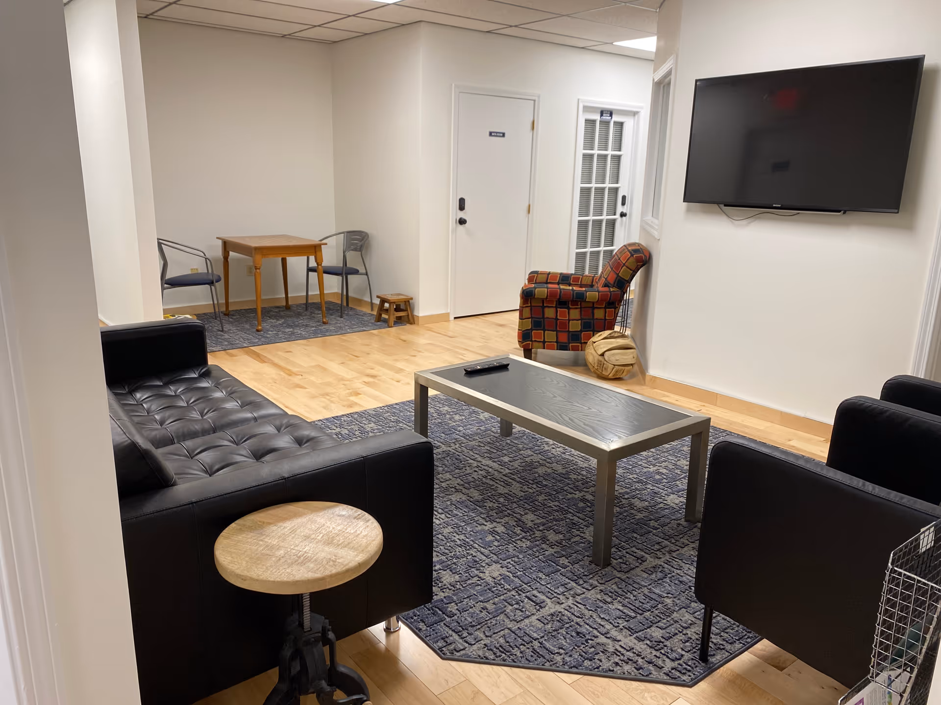 Senior living facility lounge with black leather couches, coffee table, rug, and wall TV.