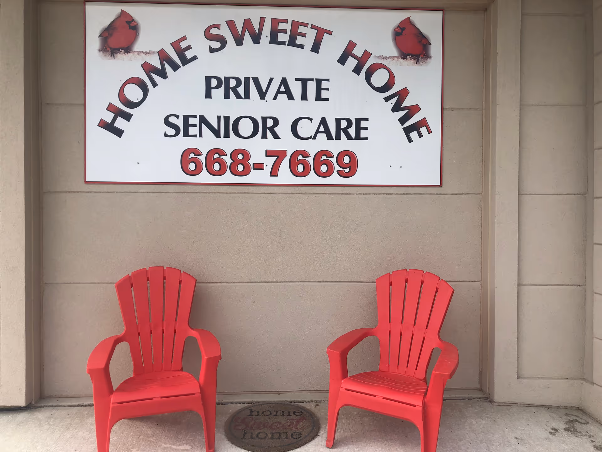 Two red Adirondack chairs sit outside a building beneath a 'Home Sweet Home' sign.