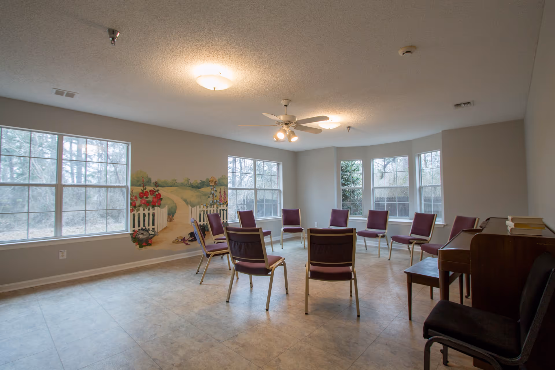 A spacious senior living common room with purple chairs arranged in a circle and a mural.