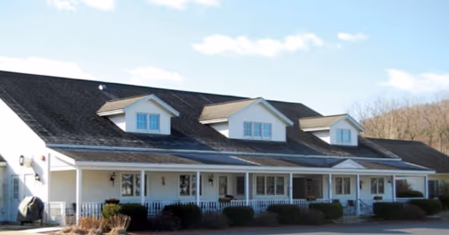 Front exterior of a single-story residential-style building with a covered porch, dormer dormer windows, and landscaping.