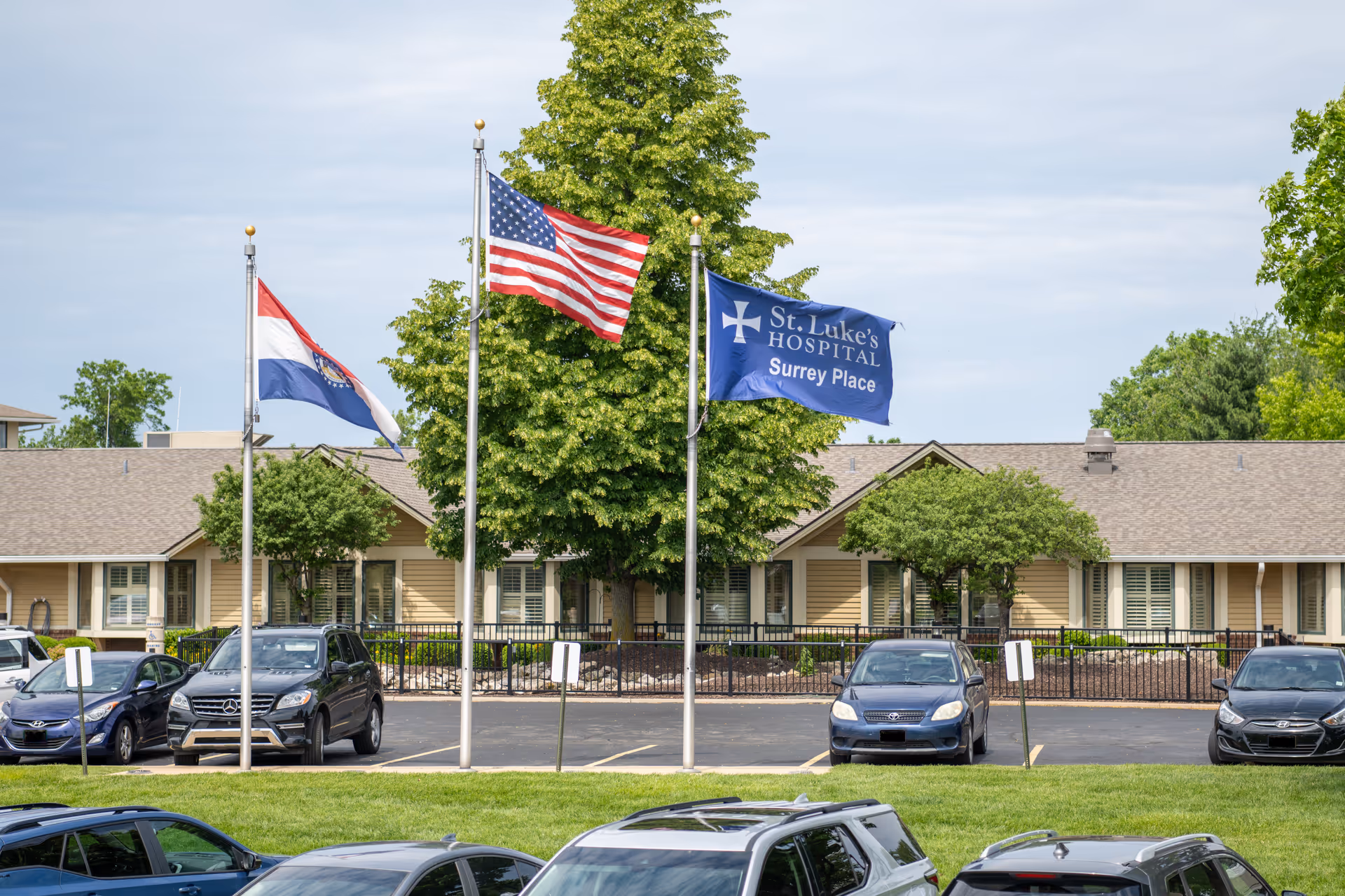 exterior view of Surrey Place St Luke's Hospital Skilled Nursing and RCF with flags and cars