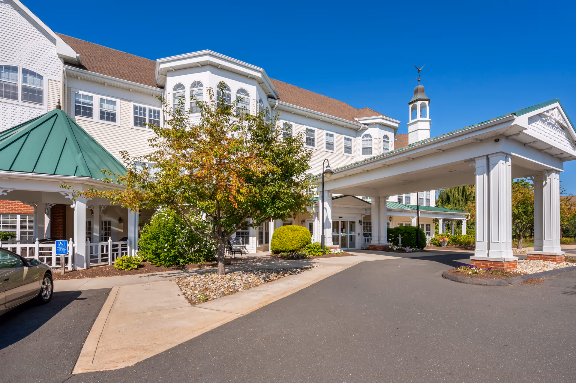 White multi-story senior living facility with a covered entrance and landscaped front courtyard.