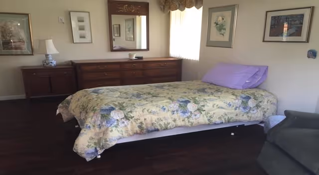 A floral bedspread covers a single bed in a cozy bedroom with dresser and artwork.