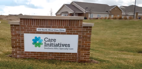 Brick sign on a grassy area displaying the address 444 North West View Drive and the logo and name Care Initiatives Southern Hills Specialty Care, with residential buildings in the background under a partly cloudy sky.