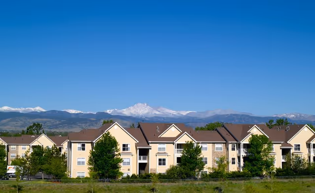 Row of beige senior living apartments with green trees and mountains in the background