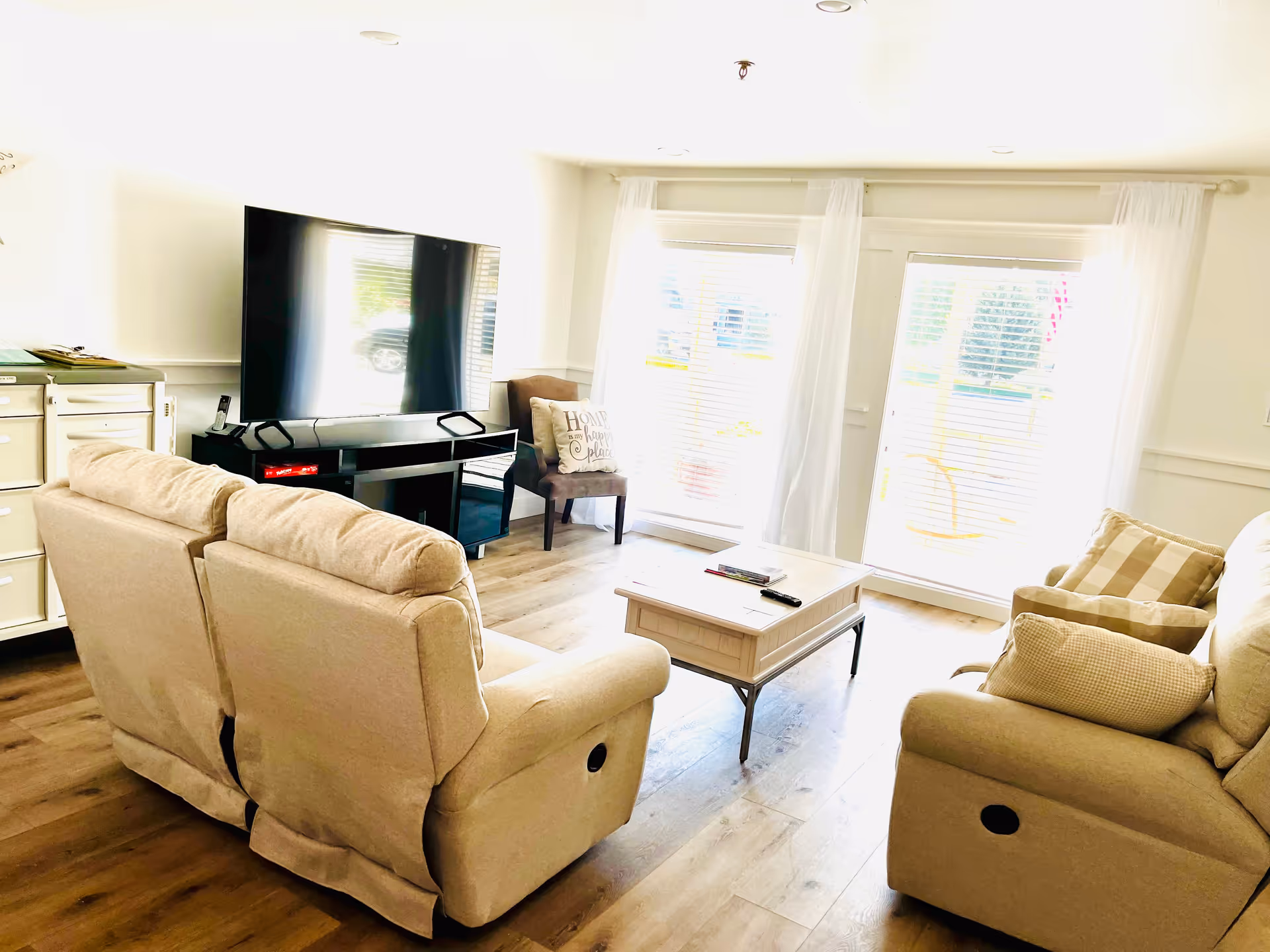 Spacious living room with beige recliners, coffee table, TV, and sliding glass doors.