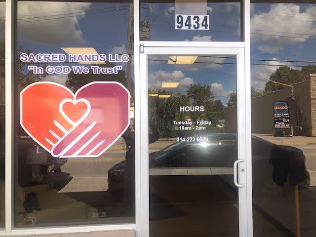 Glass storefront showing Sacred Hands LLC sign, large heart logo, and hours on the door.