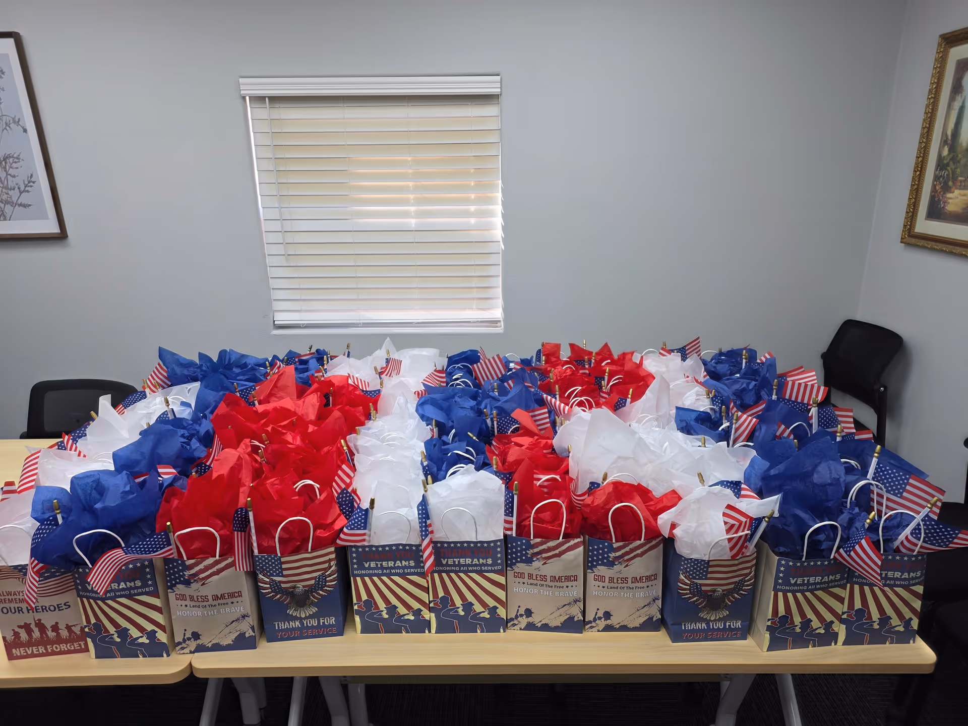 Patriotic gift bags with American flags lined up on a table in a room.