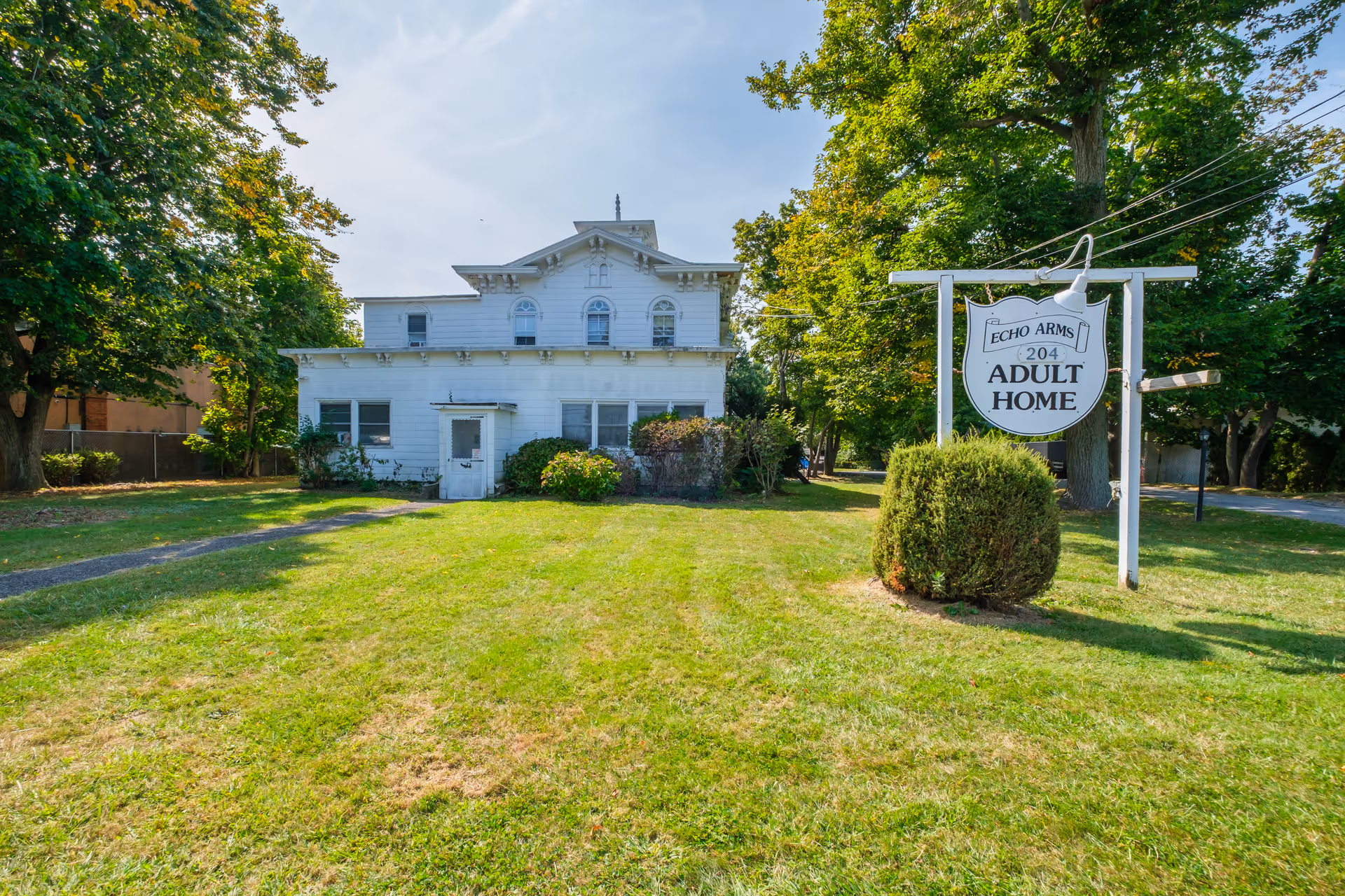 White two-story house with a front lawn and a freestanding sign reading 'Echo Arms Adult Home'.