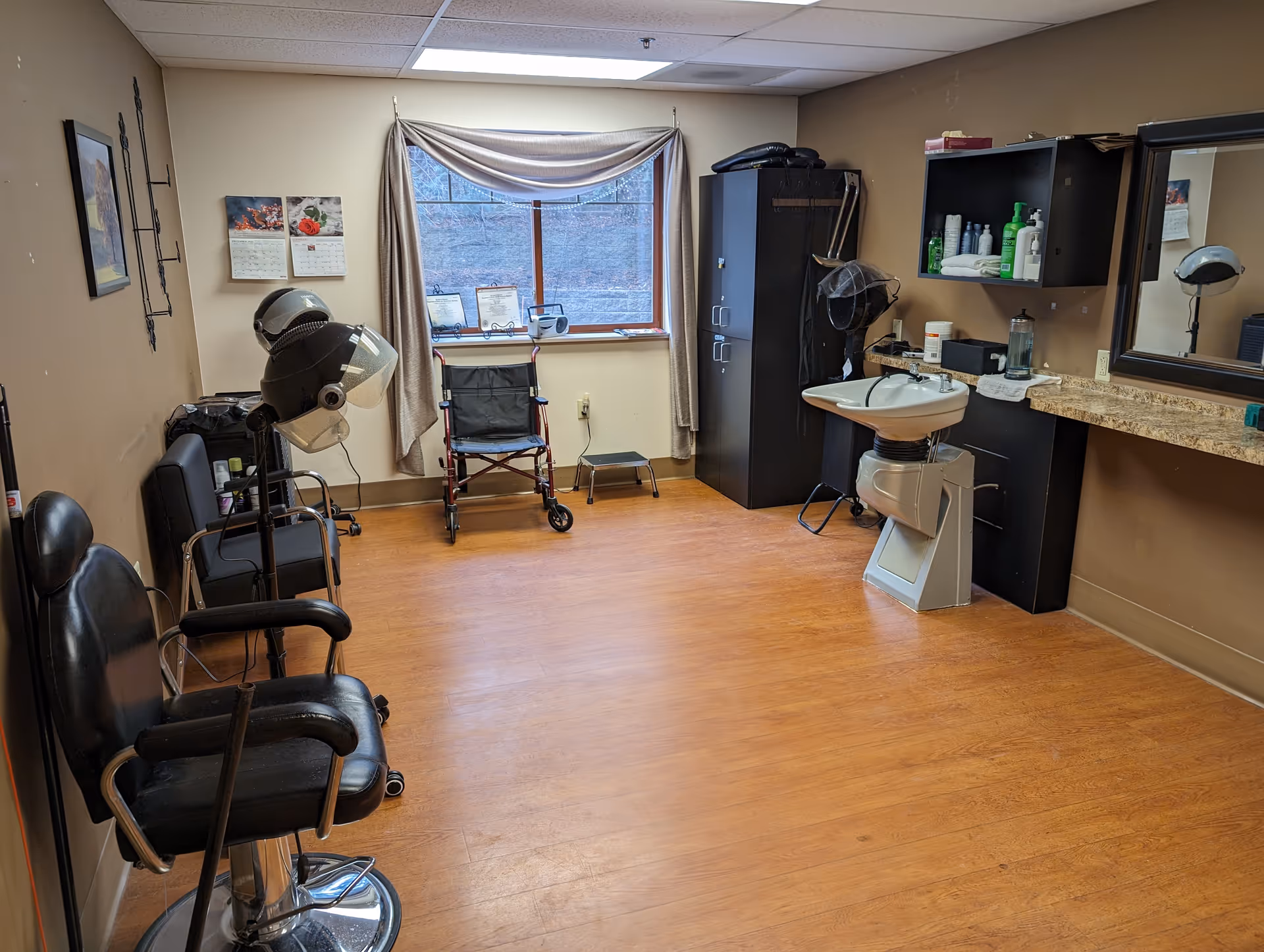 Interior salon area with styling chairs, a hooded hair dryer, sink, mirrors, and cabinets.