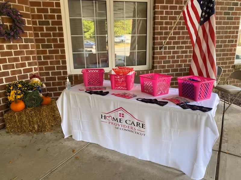 Outdoor brick porch with a promotional table, pink baskets, pumpkins, hay bale, and an American flag.