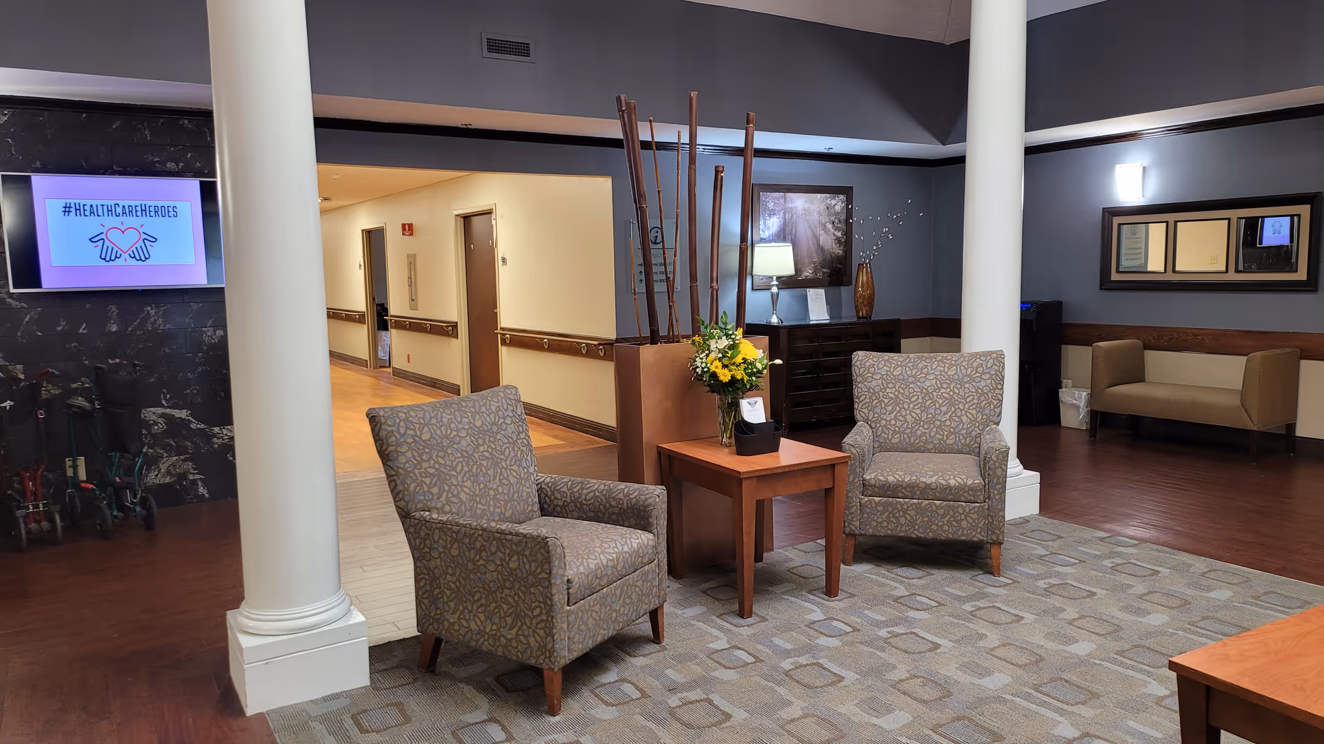 Lobby seating area with two patterned chairs, a central table with flowers, and decorative columns.