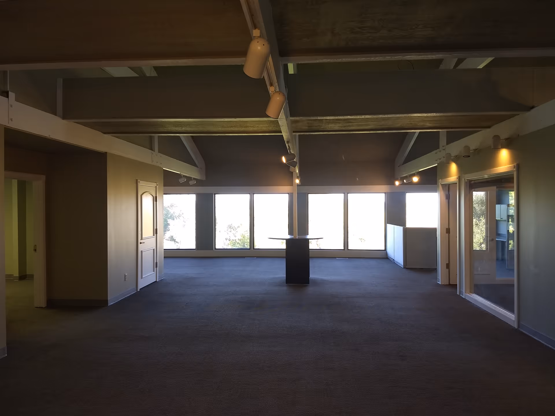 A spacious, empty interior with large windows, exposed beams, and a central pedestal table.