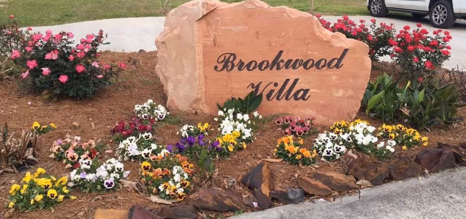 Brookwood Villa sign carved in rock, surrounded by colorful flowers.