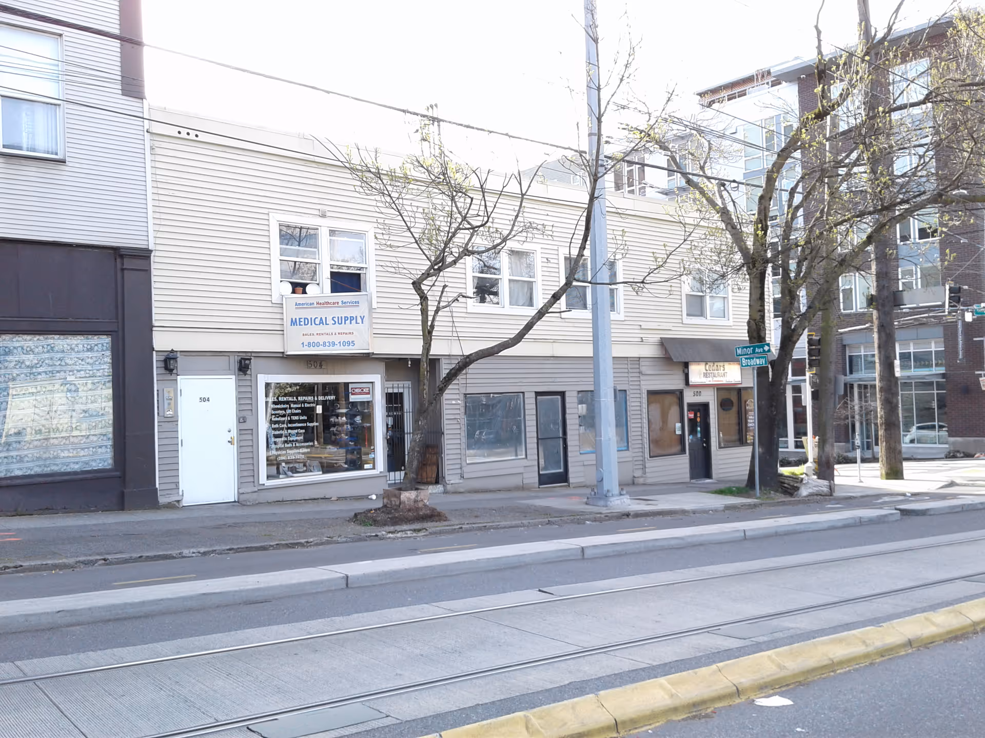 Street view of a row of storefronts with trees and a utility pole.