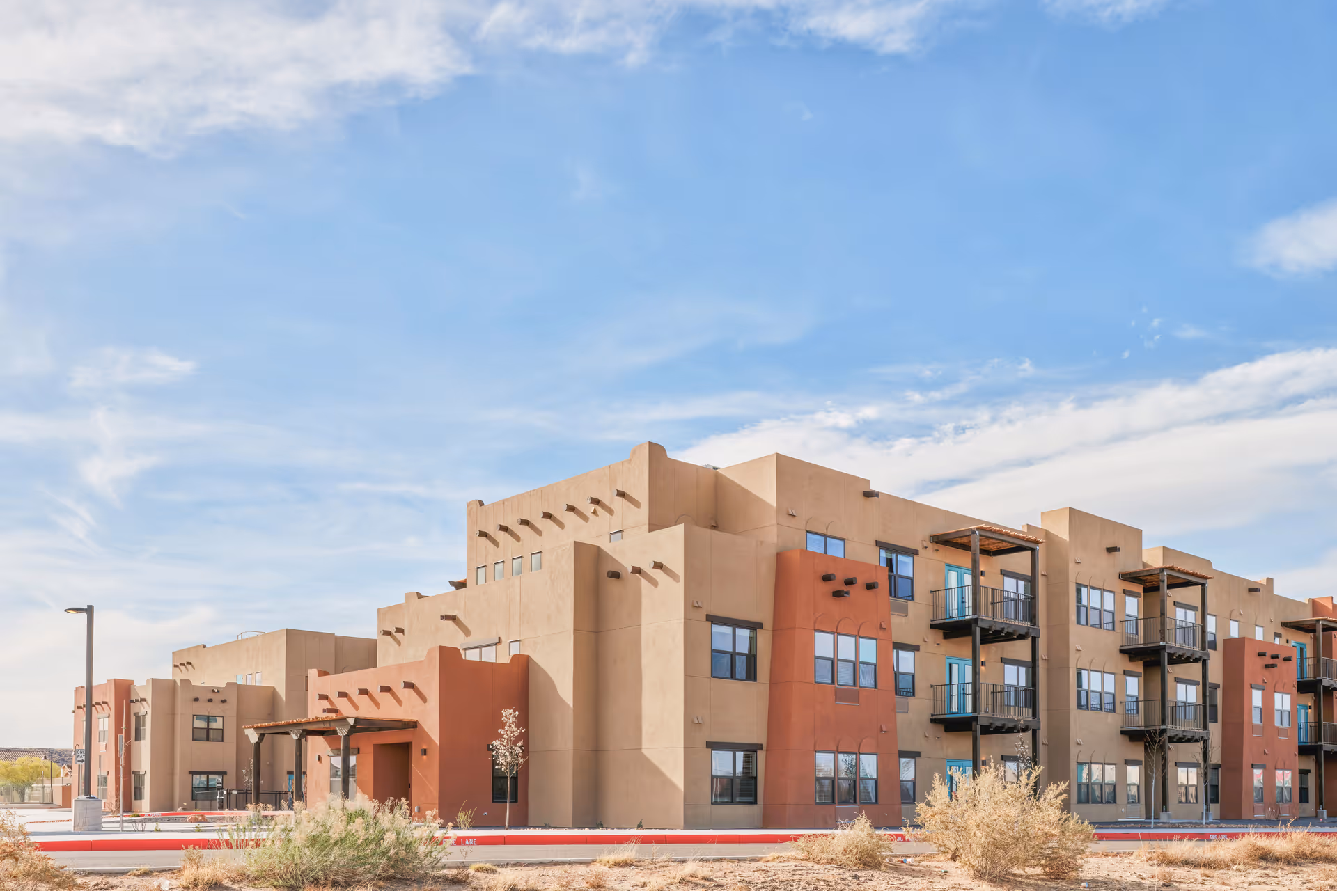 Exterior front view of a multi-story Southwestern-style apartment building with balconies under a blue sky.