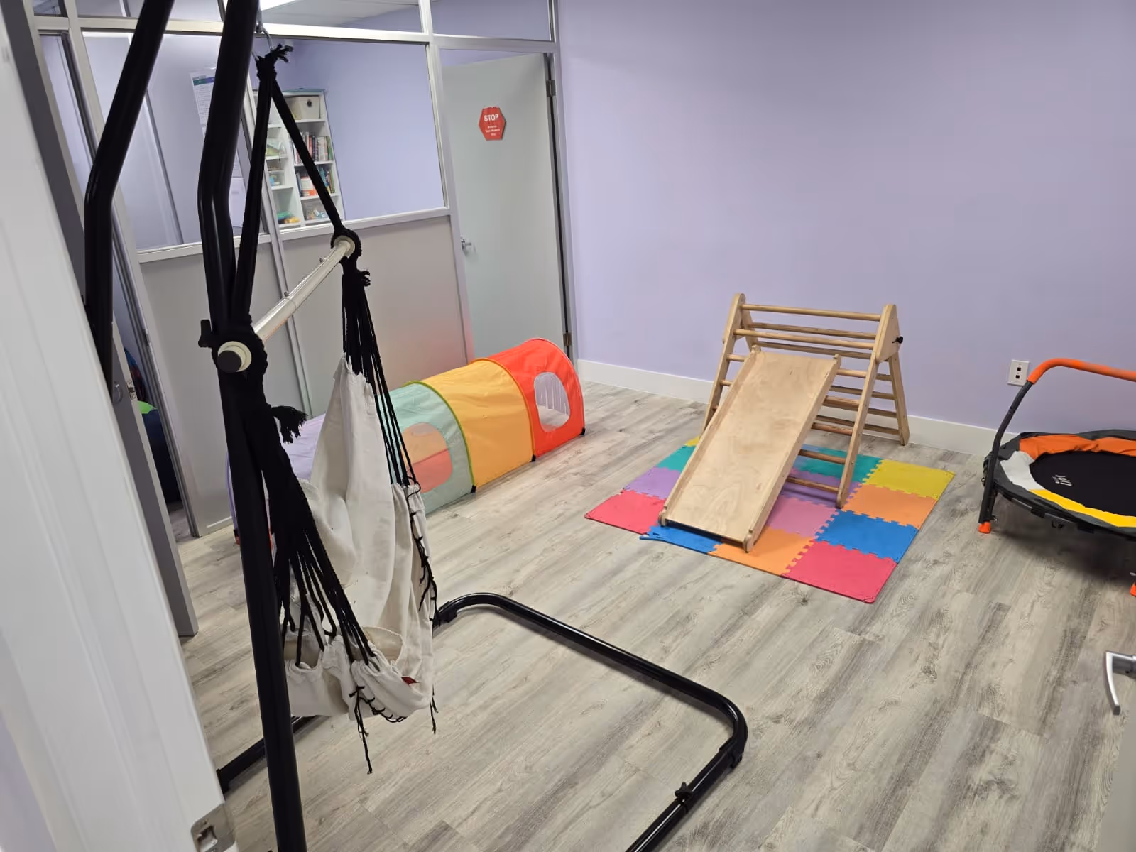 Indoor therapy room with colorful foam mats, a small slide, climbing ladder, and swing.