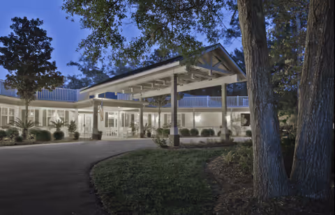 Exterior view of a senior living facility at dusk with a covered entrance, surrounded by trees and landscaped greenery.