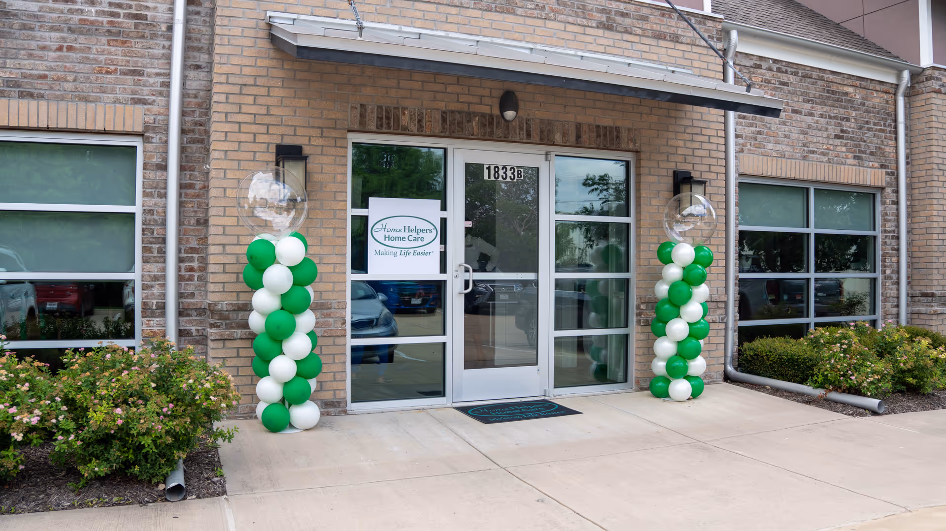 Brick building entrance with glass doors and green and white balloon columns.