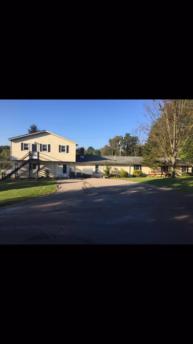 Two-story beige assisted living building with driveway and trees under blue sky