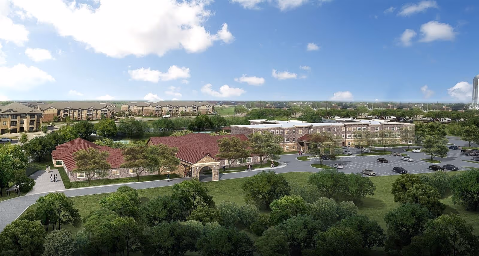 Aerial view of The Pearl Senior Living at Lewisville facility showing multiple connected buildings with red roofs surrounded by trees and greenery. There is a parking lot with several cars and a few people walking on the pathways. The sky is blue with scattered clouds.