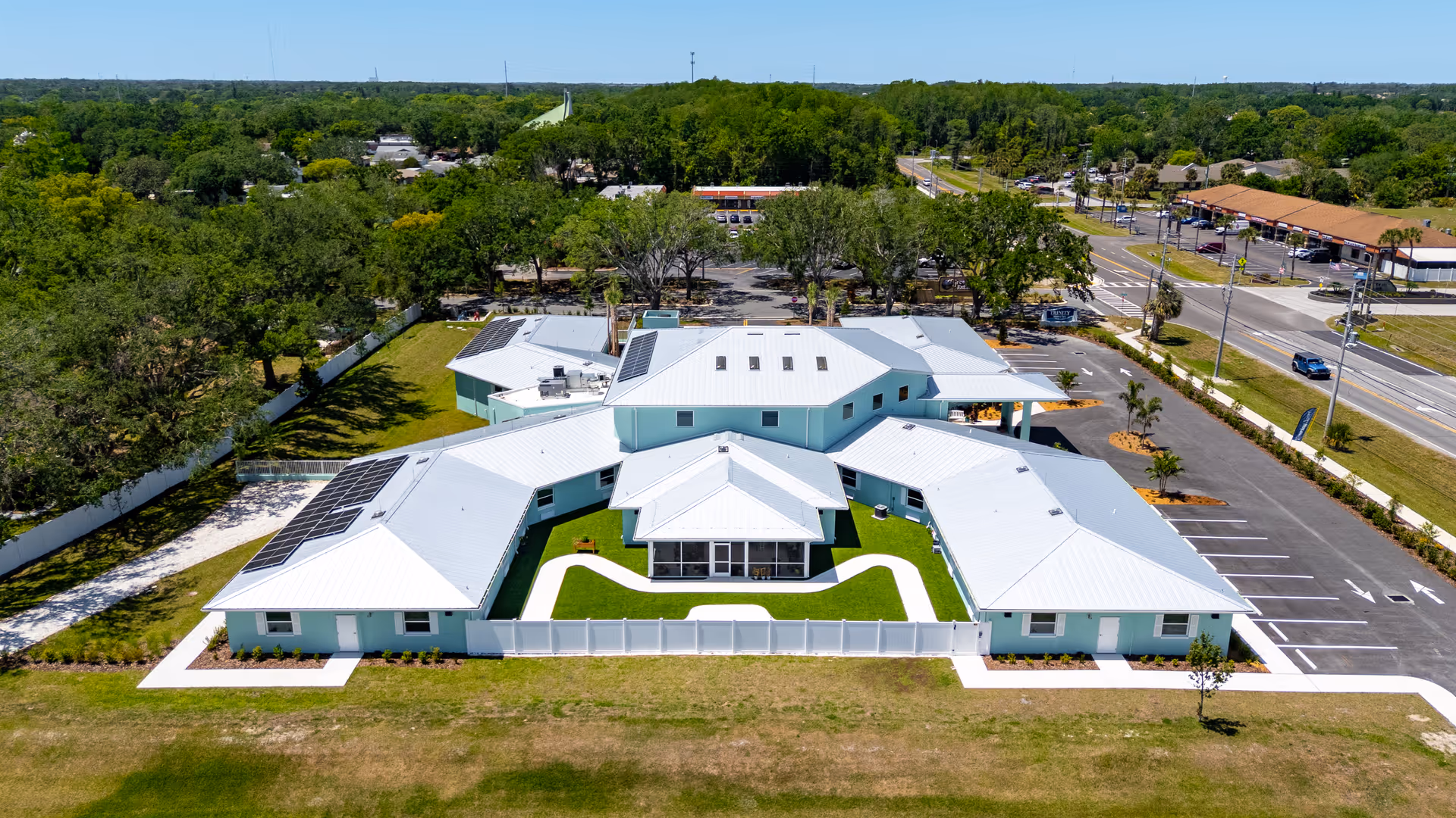 A large light blue memory care facility with a white roof and central courtyard, aerial view.