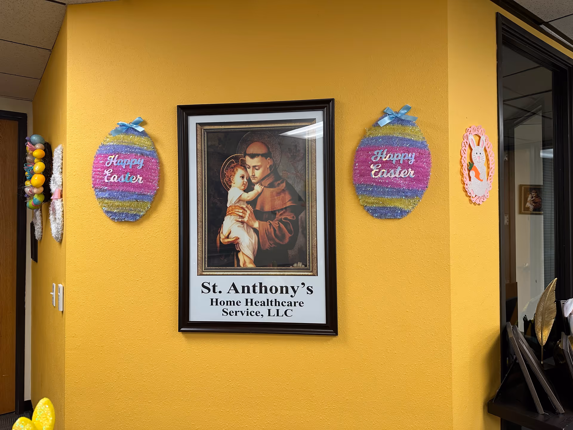 Framed St. Anthony's Home Health Care sign on a yellow interior wall with Easter decorations.