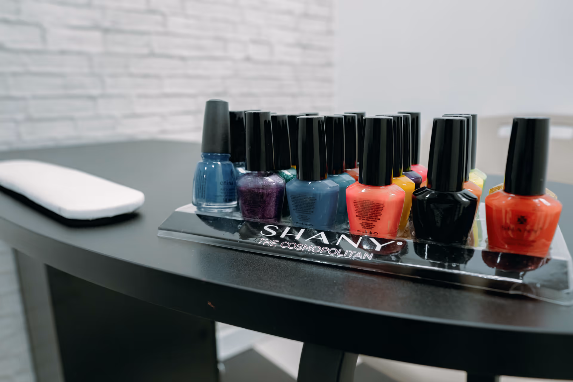 Row of colorful nail polish bottles on a curved black salon table.