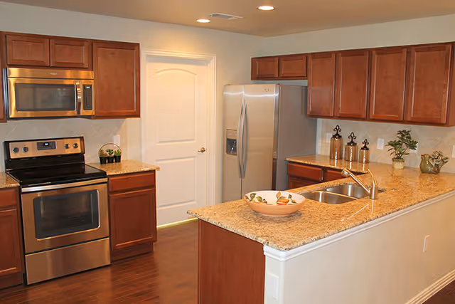 Kitchen with granite counters, stainless appliances, island sink, and wooden cabinets.