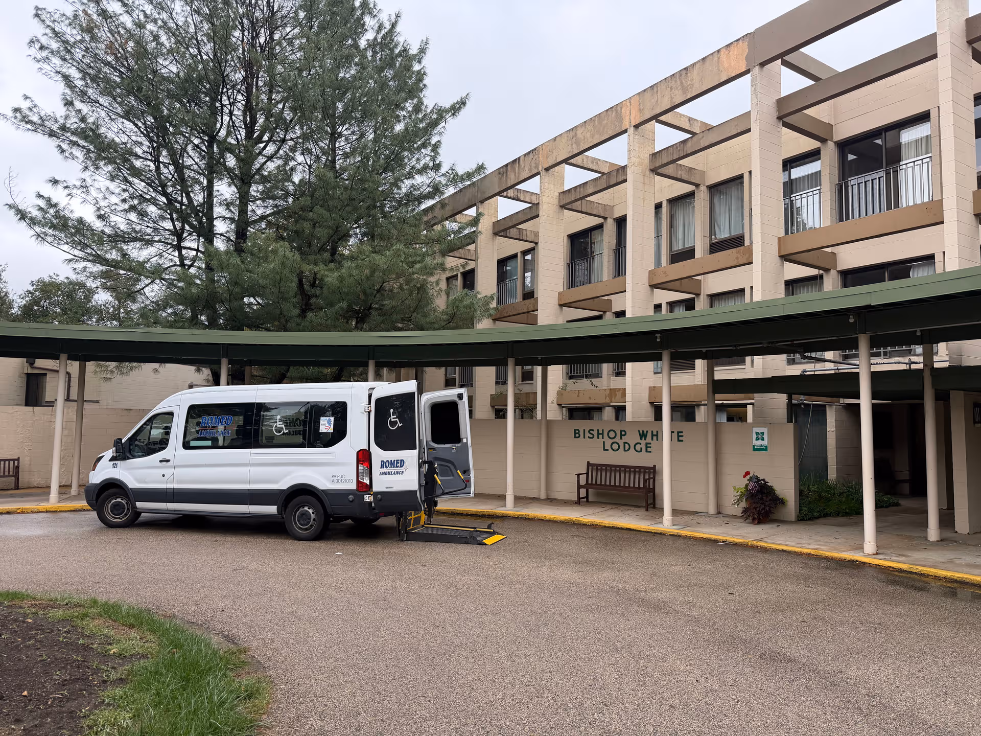 Exterior view of Cathedral Village building entrance with a wheelchair-accessible van under a green canopy.