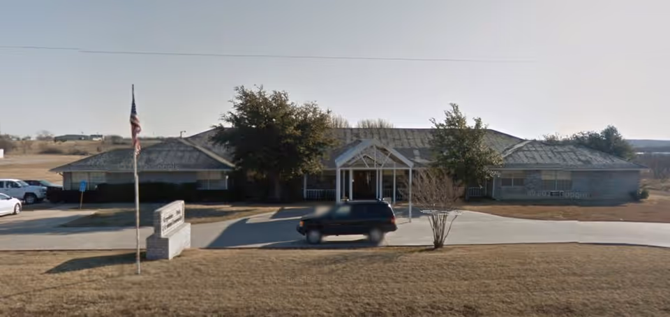 Front view of Greystone Park senior living facility with entrance, flagpole, and parked car.