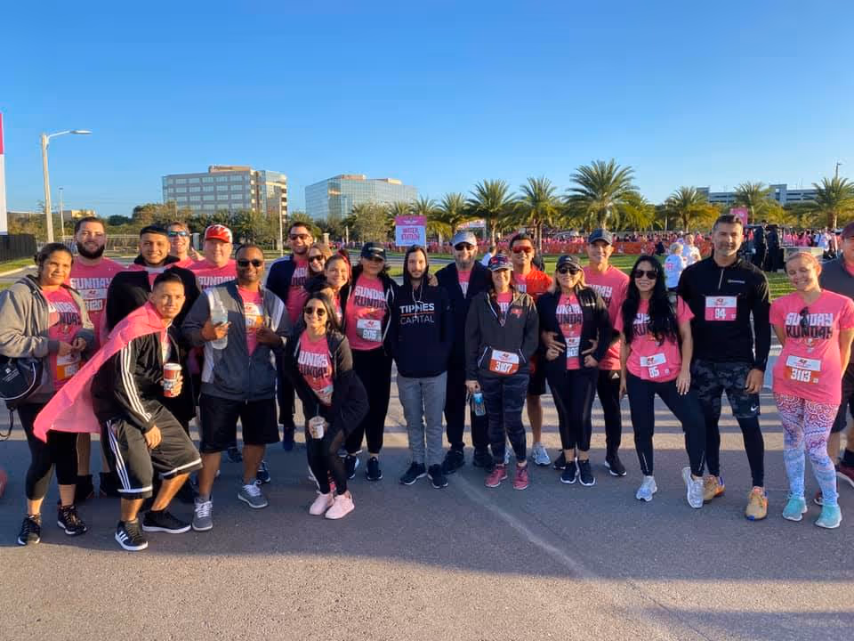 Group of people in pink shirts posing together outdoors at a sunny charity event.