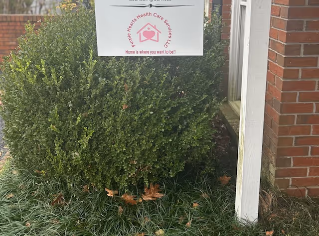 Sign for Purple Hearts Health Care Services, LLC beside brick building, surrounded by shrubs.