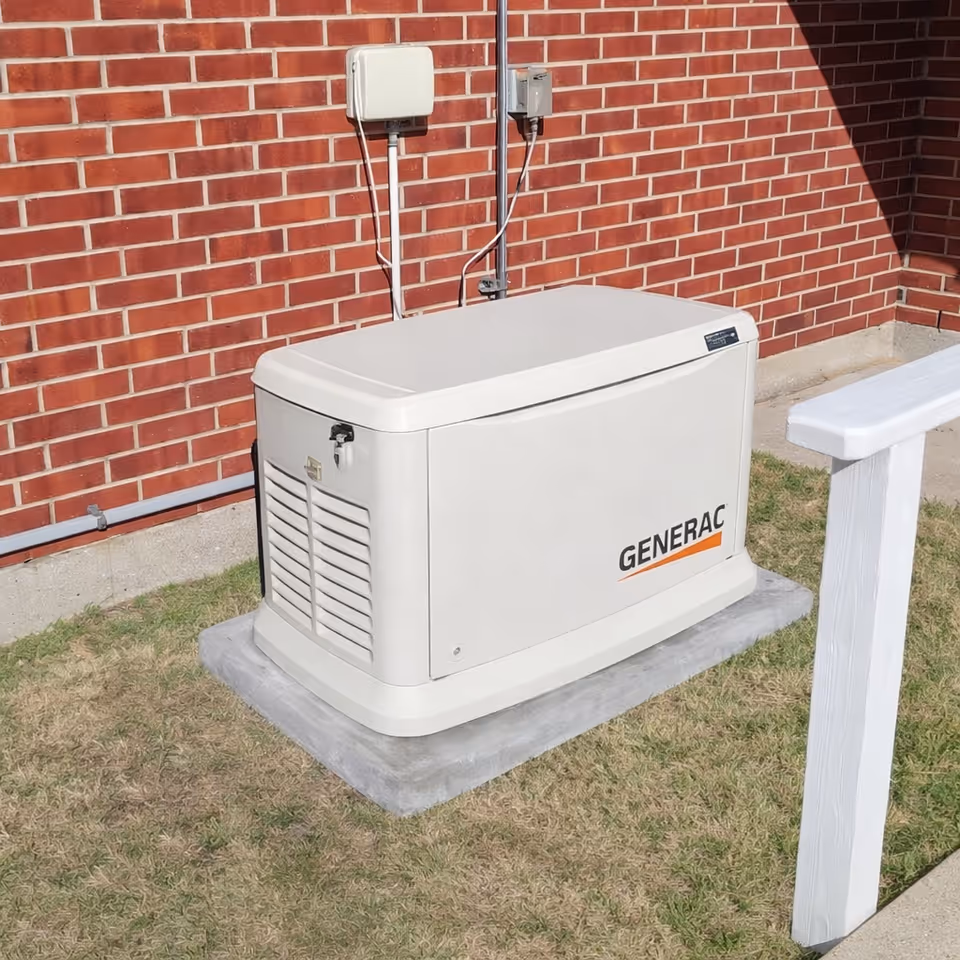Generac generator sits on a concrete pad beside a red brick building outdoors.