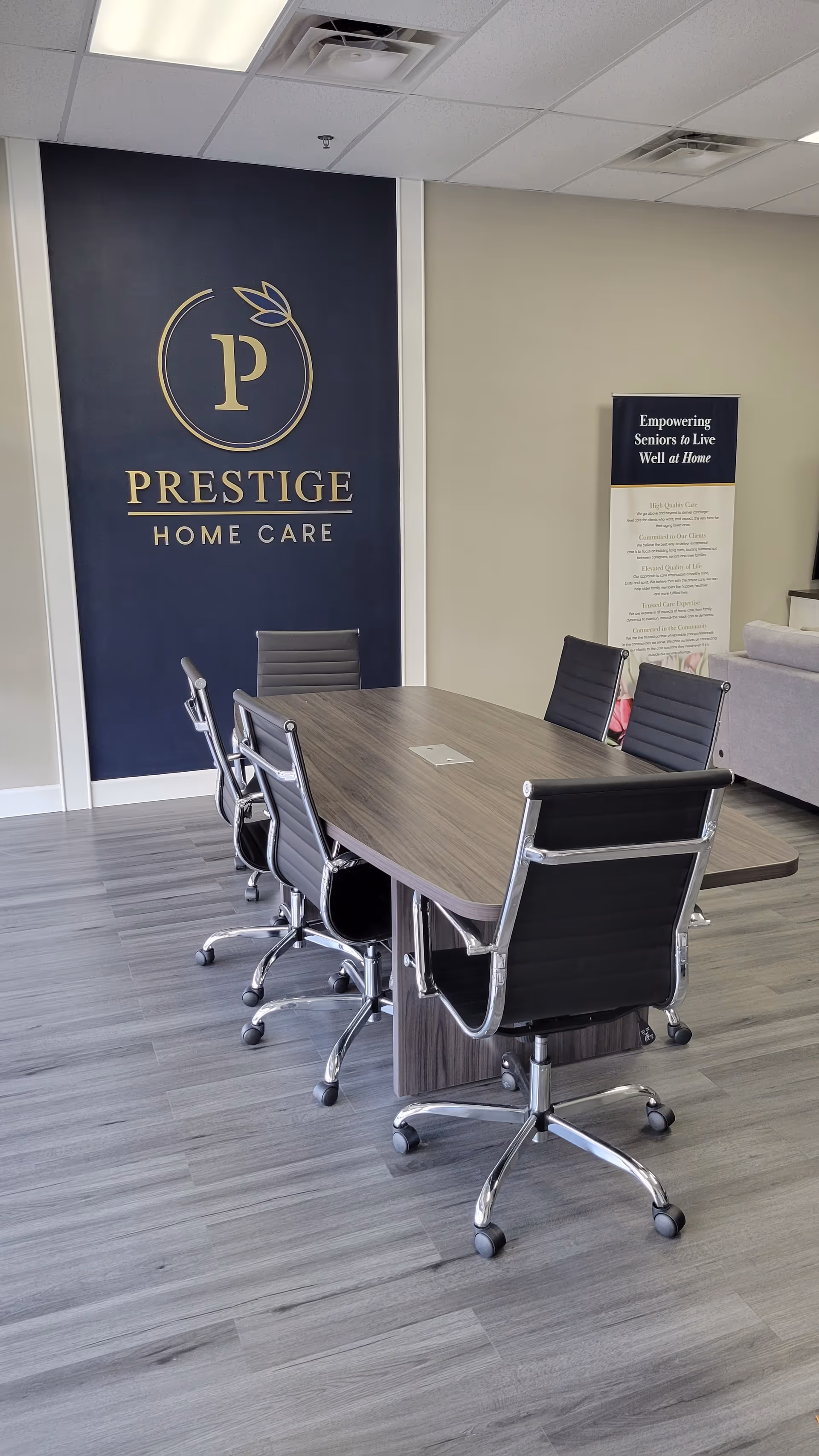 Modern meeting room with a wood table, black chairs, and Prestige Home Care branding.
