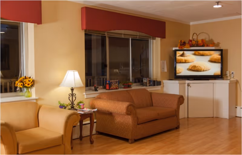 Cozy senior living room with beige furniture, a TV, and a large window.