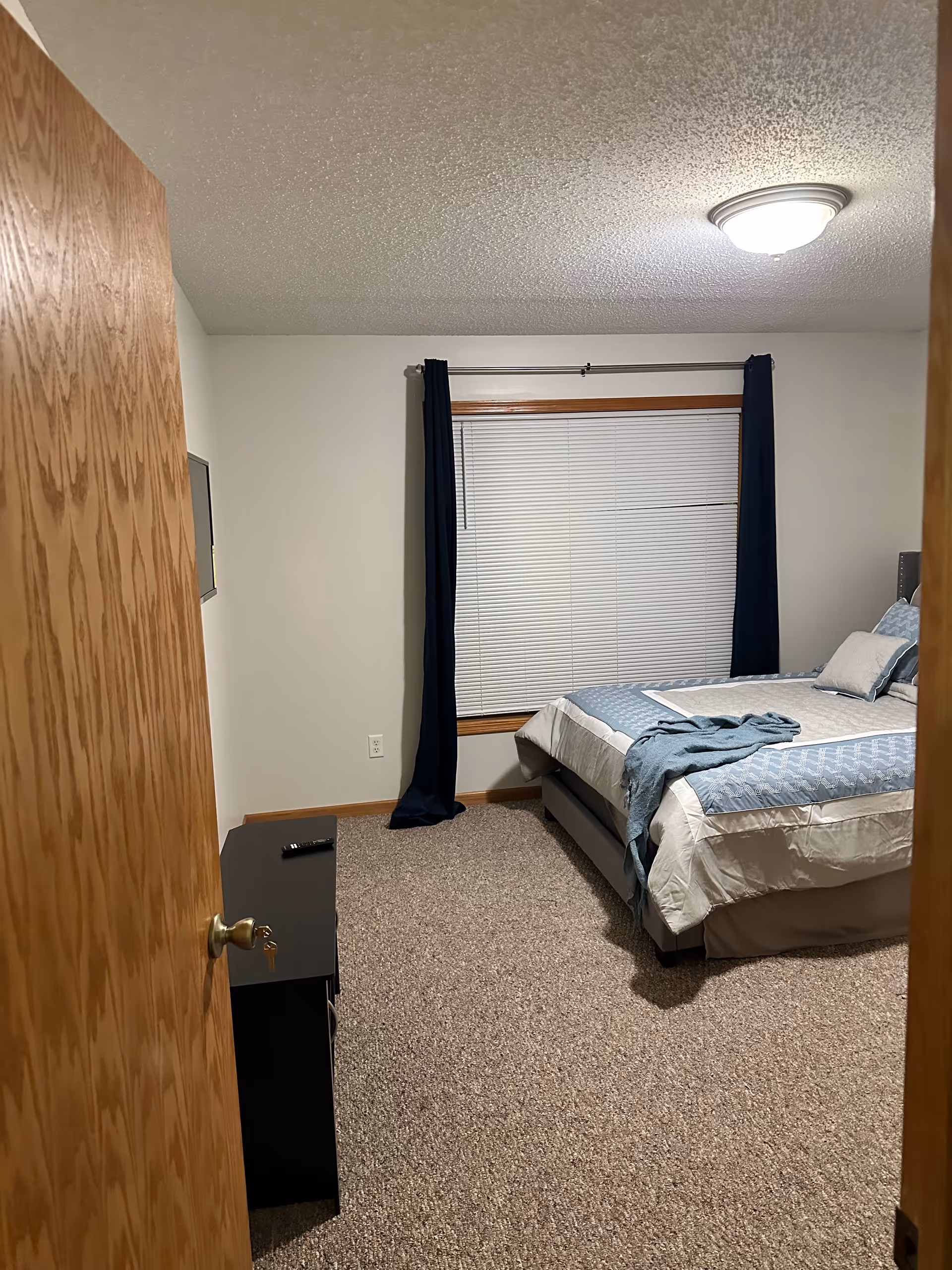 A tidy bedroom with a bed, window blinds, curtains, and a dresser in a senior facility.