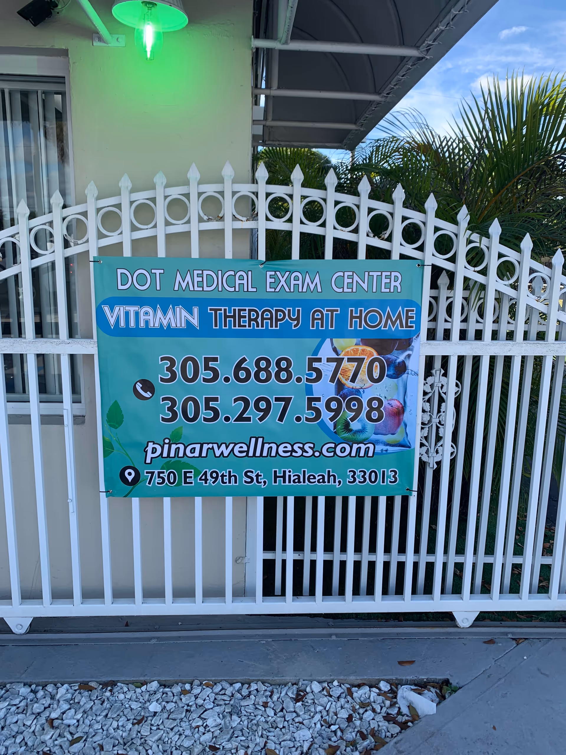 Exterior view of a white fence with a teal banner advertising medical exam and vitamin therapy.