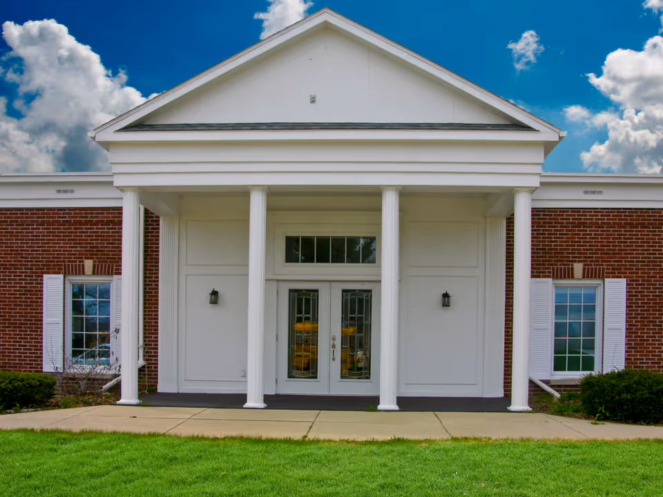 Front view of a brick-sided building with white columns, double doors, and a blue sky.