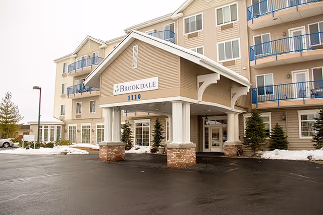 Front entrance of a multi-story senior living facility with a covered porte-cochere.