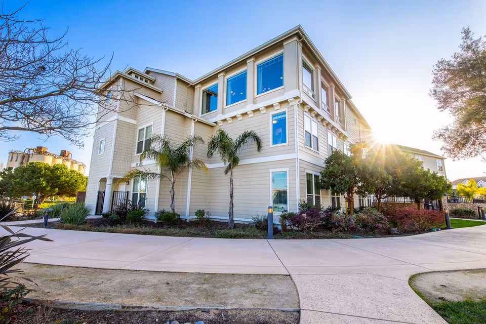 Sunlit, multi-story senior living building with manicured landscaping and curved walkway.