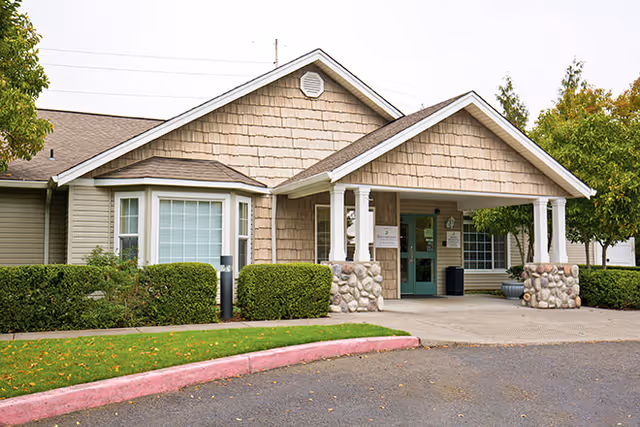 Front entrance of a single-story senior living facility with a covered porch, stone pillars, and landscaping.