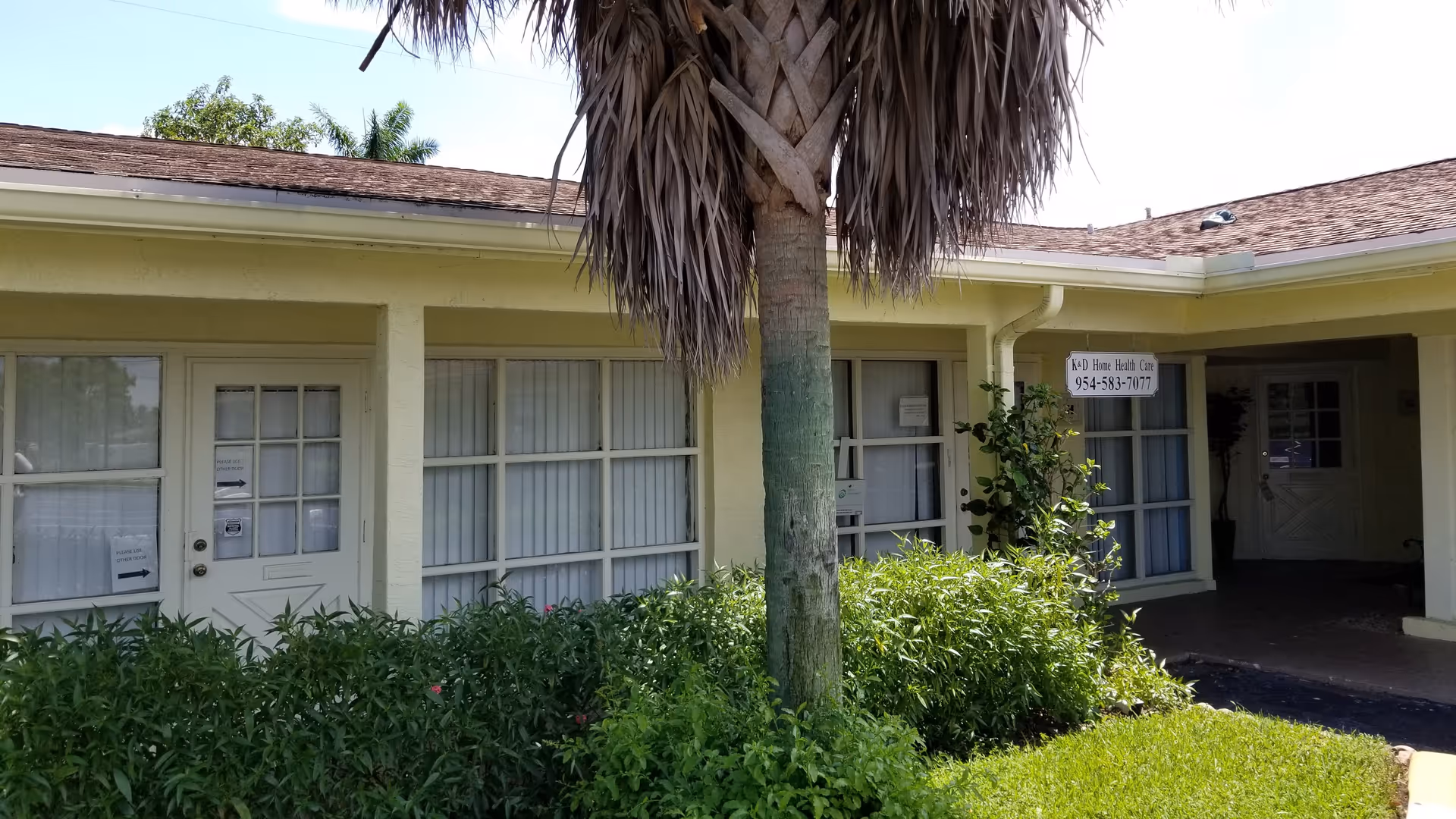Exterior view of a single-story senior care facility with large windows and a palm tree.