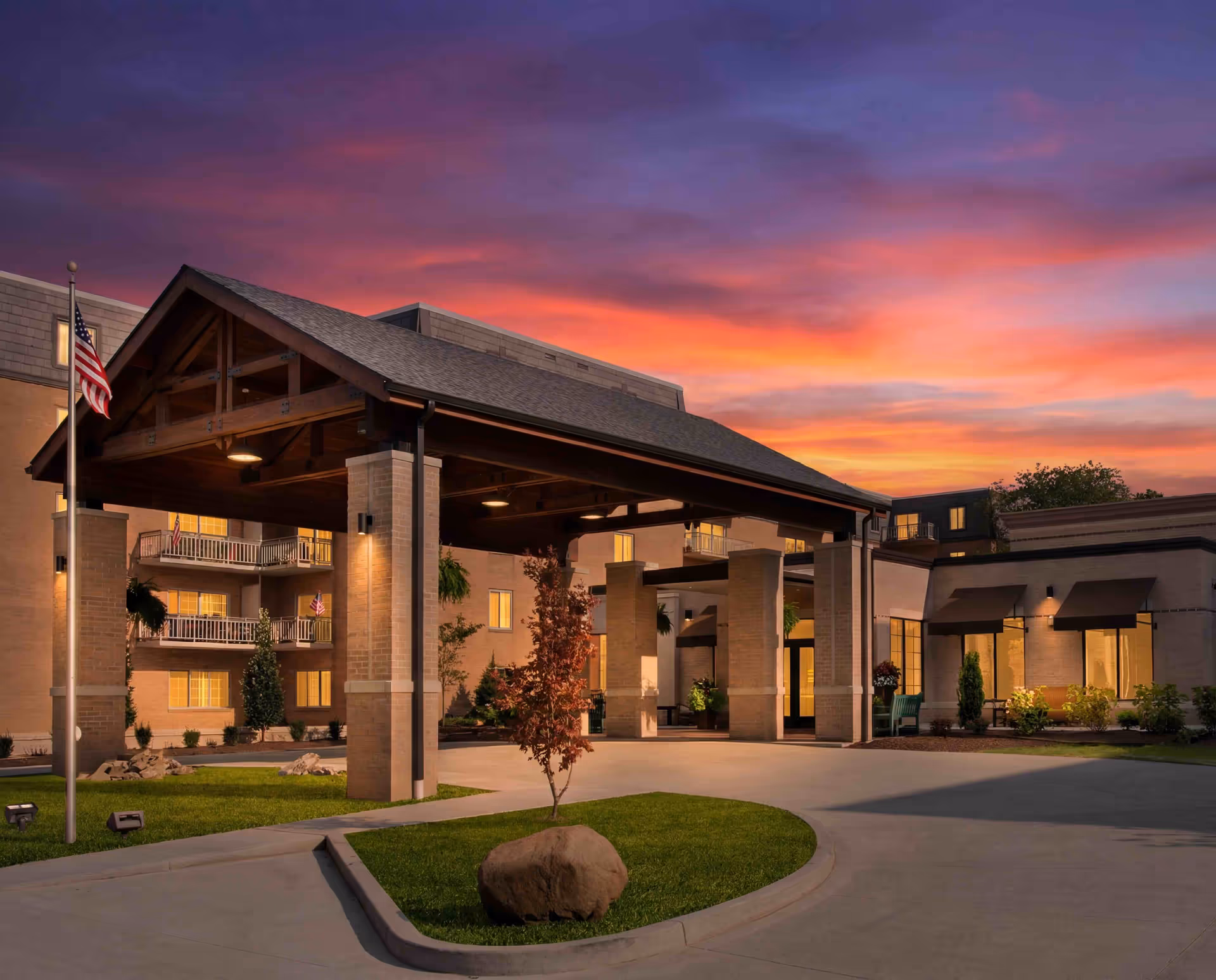 Sunset sky over Normandy Senior Living entrance with a wide porte-cochere and American flag
