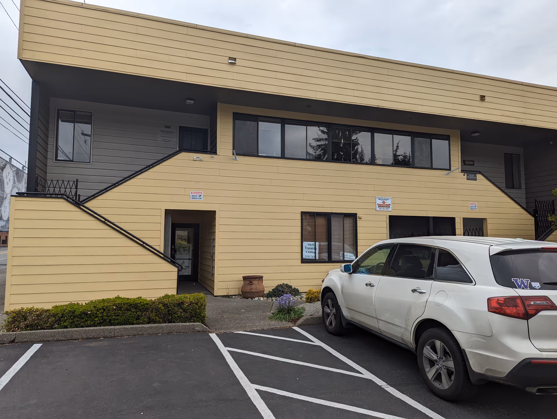 Two-story beige building with stairs, windows, and a white SUV in the parking lot.