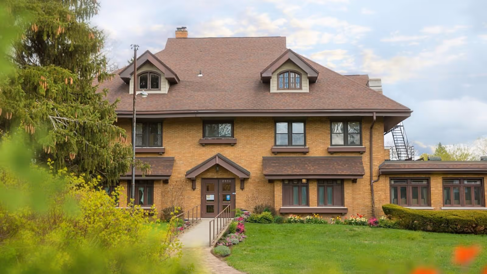 Brick senior living facility with a brown roof and manicured lawn in front.