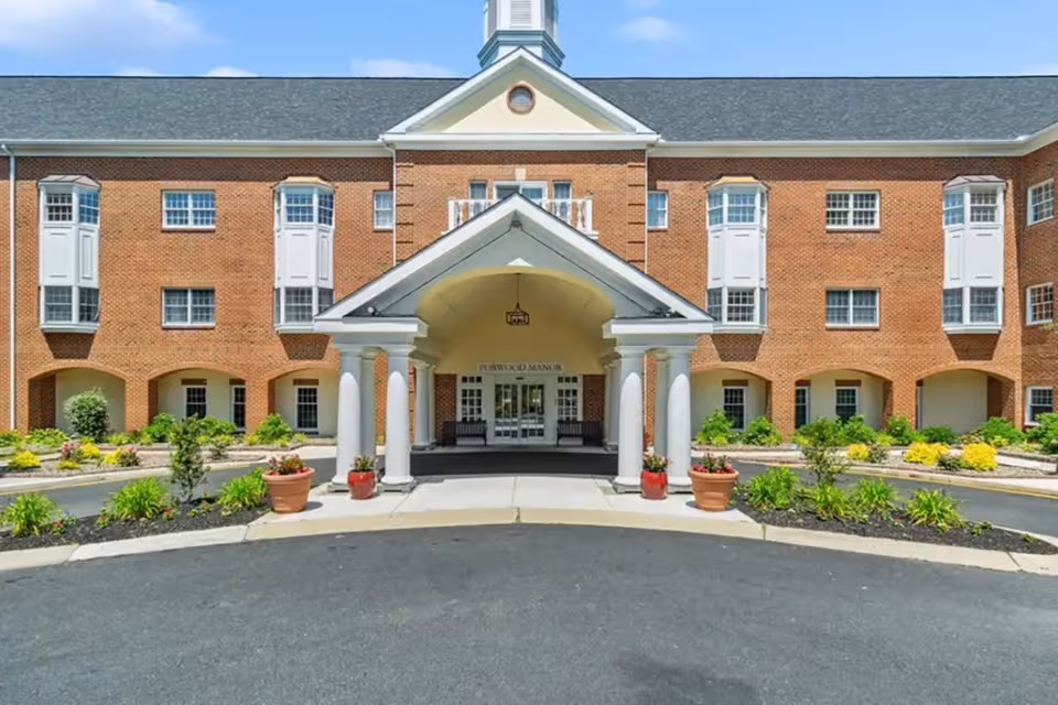 Front entrance of Forwood Manor, a brick senior living facility with columns and landscaping.